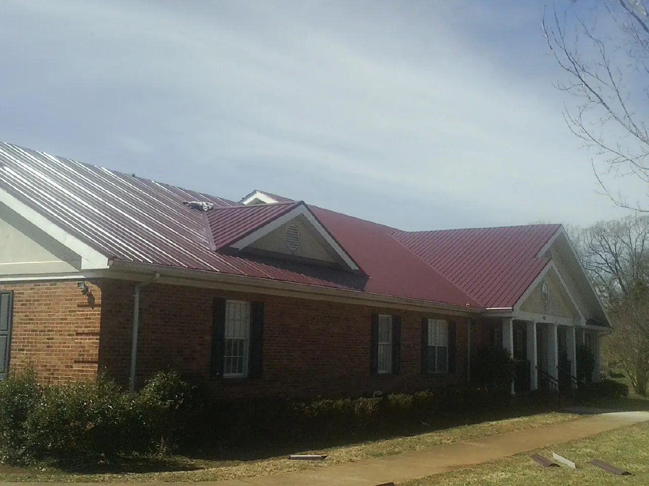 Red metal roof with gabled entries on a long brick building, from a Hail Damage Roof Repair job in Dearing